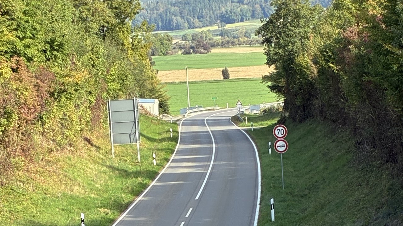 Das Foto zeigt die L 207 die vor einer Rechtskurve durch das Ende eines Waldstücks führt. Rechts sieht man ein Tempobegrenzungsschild mit der Aufschrift 70; darunter ein Überholschild.