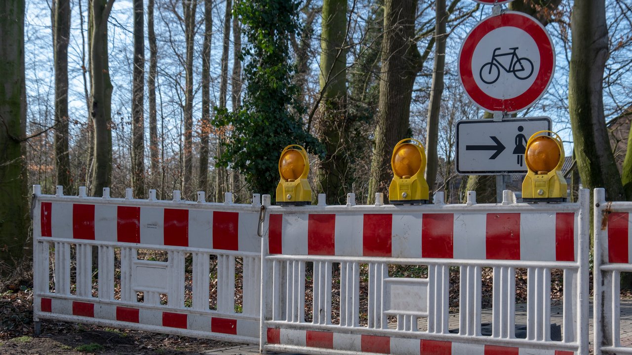 Das Bild zeigt eine rot-weiße Absperrung in einem Wald und ein Fahrradverbotsschild