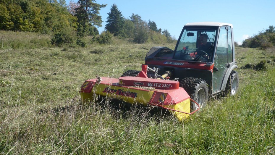 ein Mähgerät fährt über eine Wacholderheide