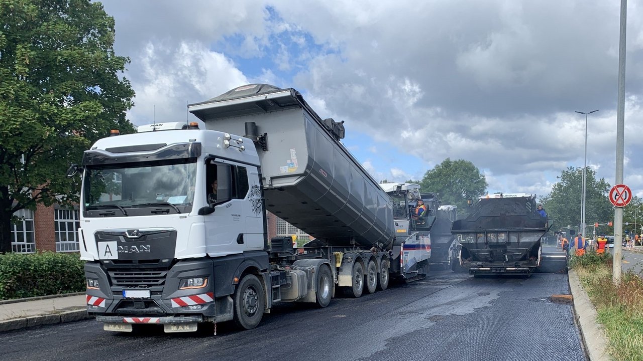 Asphaltierarbeiten auf der B 464. Ein Laster kippt die Ladefläche hoch und Asphalt wird abgeladen.