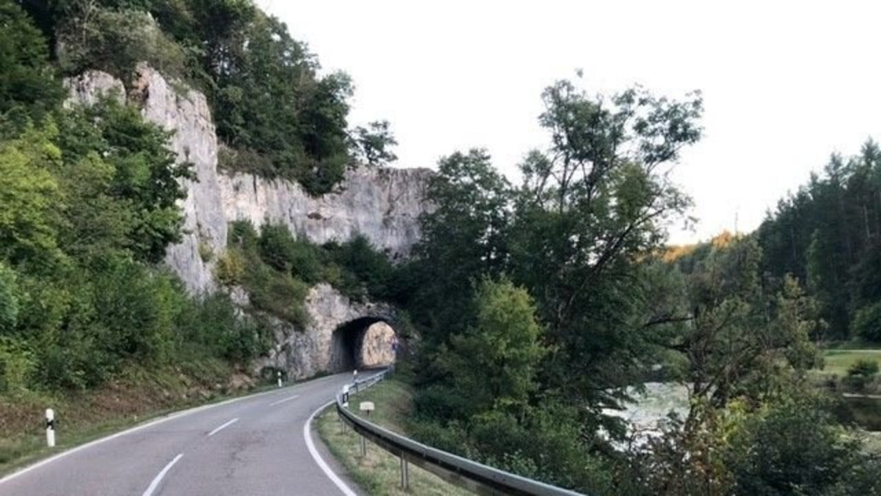 Das Bild zeigt die eine Kurva auf der L 277 zwischen Thiergarten und Laiz vor einem Felstunnel; rechts sieht man einen Fluss, Bäume und Wiesen