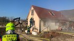 Ein Feuerwehrmann von hinten im Vordergrund. Im Hintergrund klettert ein Helfer des Technischen Hilfswerks über eine Leiter in den ersten Stock eines Gebäudes, aus dem Rauch kommt. 
