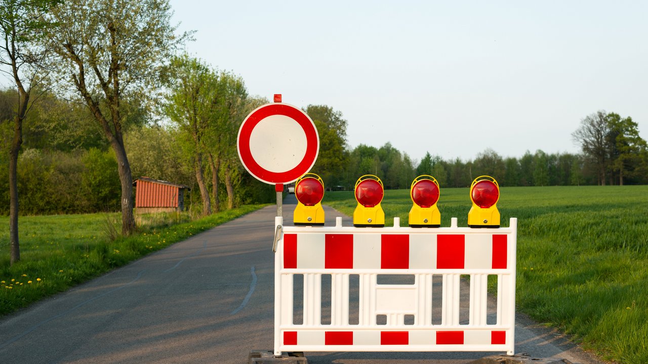 Strassenbarken und ein Schild sperren eine Straße auf dem Land ab. 