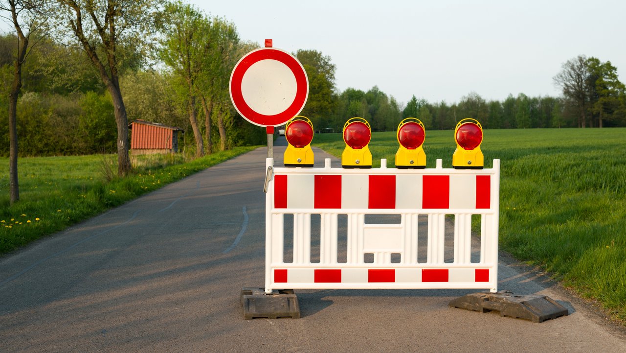 Strassenbarken und ein Schild sperren eine Straße auf dem Land ab. 