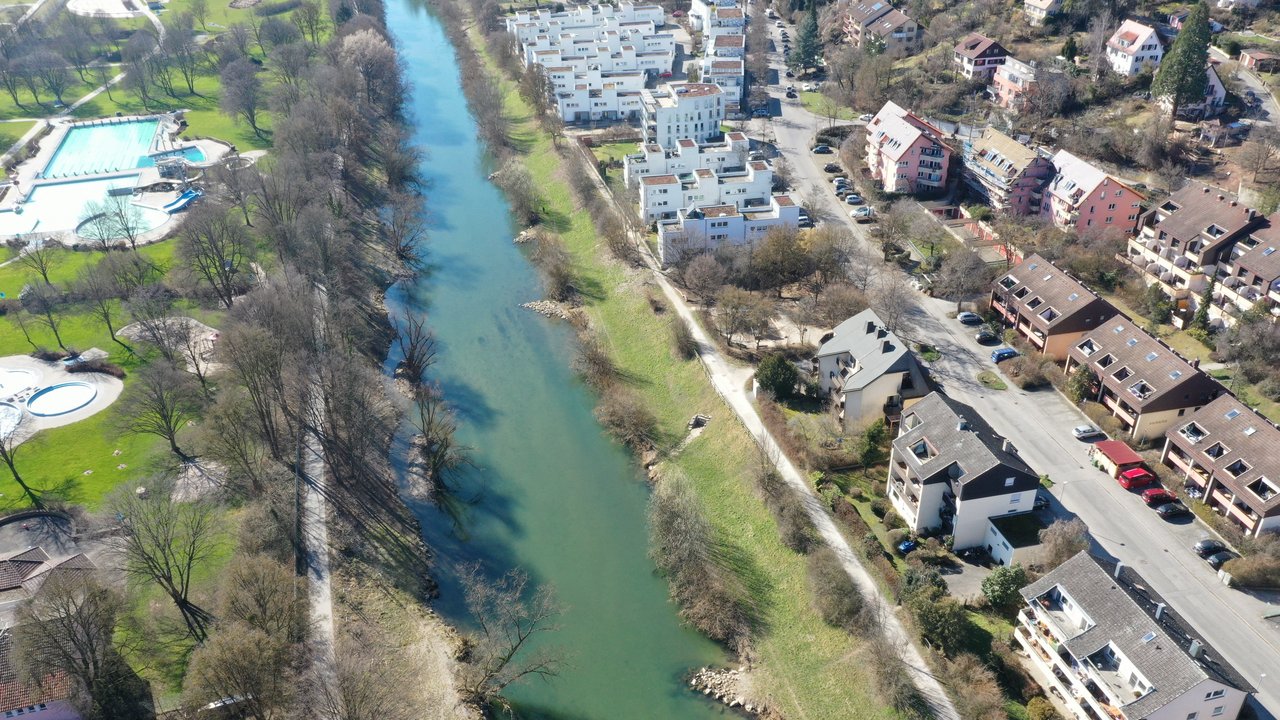 Das Foto zeigt den Neckar von oben. Links davon die Becken des Freibad Tübingen und rechts die Häuser einer Wohnsiedlung