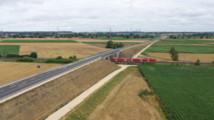 Brücke über die Bahn Luftbild einer Straßenbrücke, die über die Gleise führt. Auf den Gleisen fährt ein roter Regionalzug.
