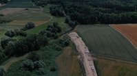 Luftbild eines Erddamms, der bis an die Ufer eines kleinen Flusses aufgeschüttet ist. 