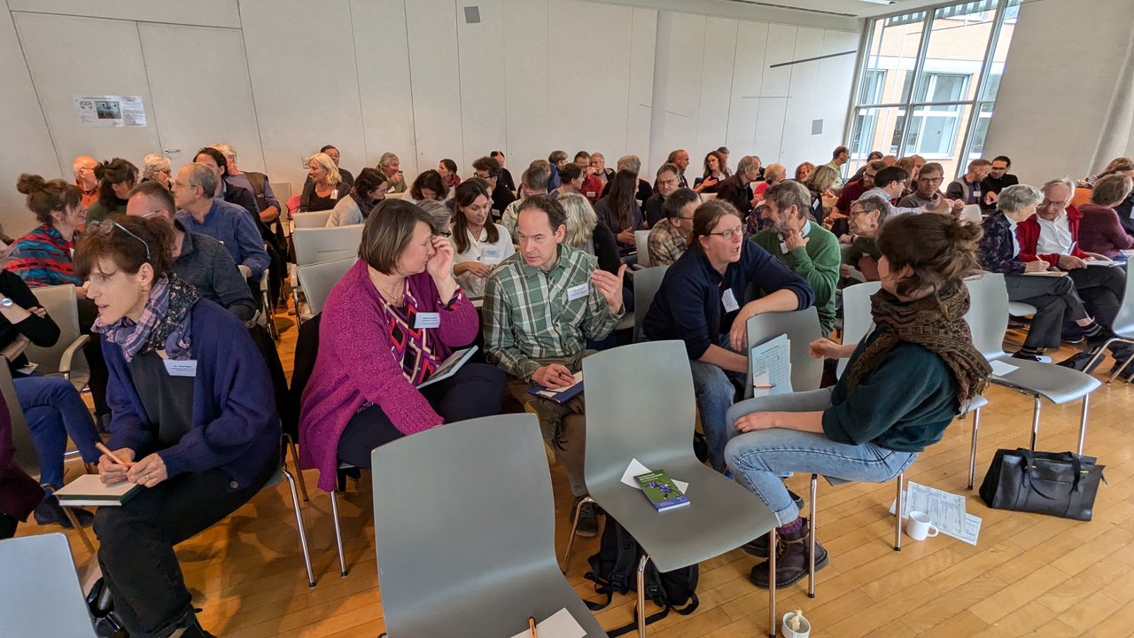 Das Foto zeigt mehrere Personen mit Namensschildern bei einem Workshoph in einem großen Besprechungsraum
