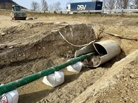 Ein Wellstahl-Rohr kommt unter einer Straße hervor. In einem Graben läuft ein grünes Kunsttoffrohr in Richtung des Durchlasses. 