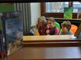Gemeindebücherei Baindt 3 Kinder sitzen hinter Bücherregalen in der Gemeindebücherei Baindt