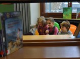 Gemeindebücherei Baindt 3 Kinder sitzen hinter Bücherregalen in der Gemeindebücherei Baindt