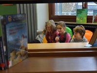 3 Kinder sitzen hinter Bücherregalen in der Gemeindebücherei Baindt