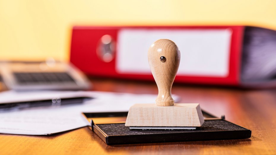 Schreibtisch mit Stempel und Büromaterial Stempelkissen mit Stempel und rotem Ordner im Hintergrund