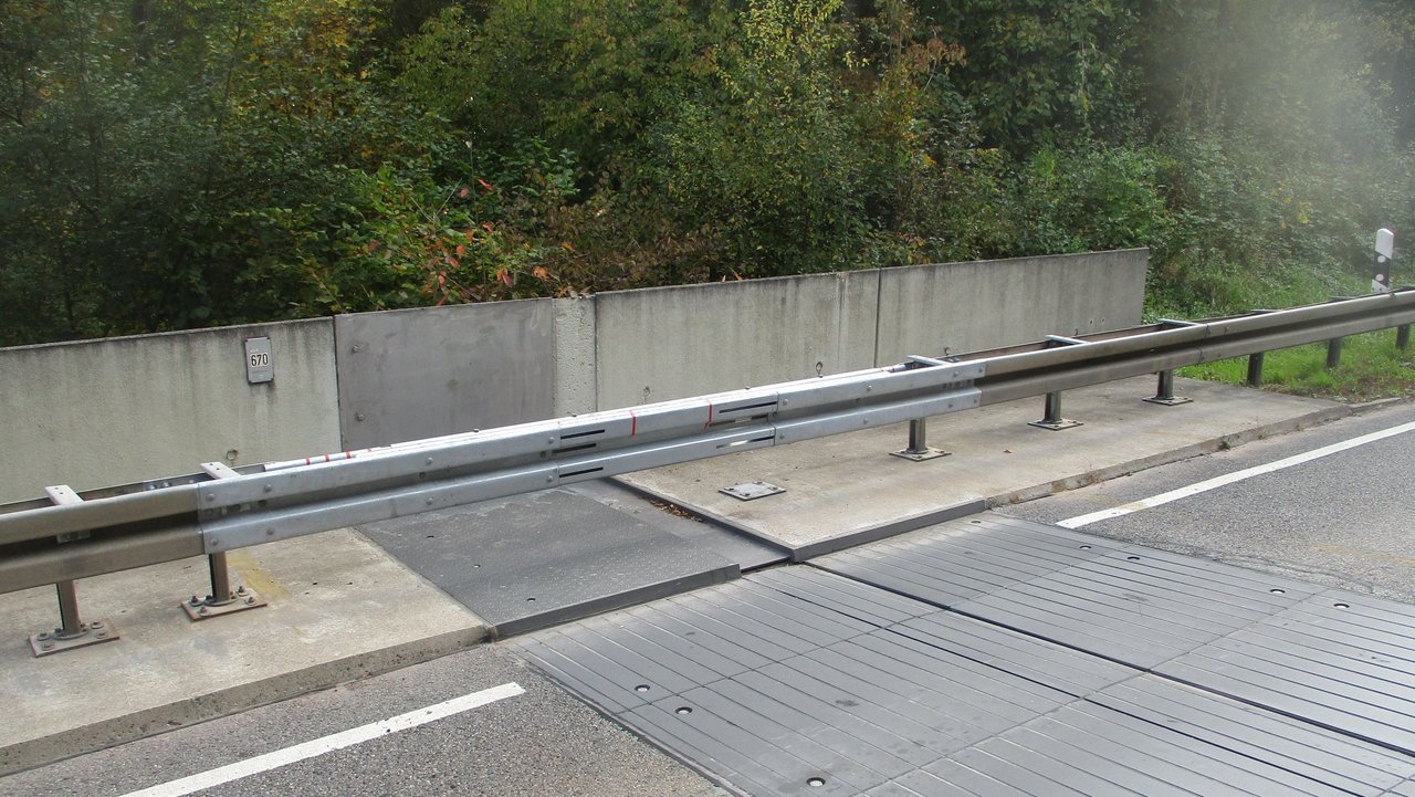 Das Foto zeigt die Fahrbahnübergangskonstruktion von der B 464 auf das Neckartalviadukt. Man sieht Leitplanken und Gestrüpp an der Seite.