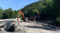 Bagger stehen am Rand einer staubbedeckten Brücke, aufgebrochene Betonteile liegen herum