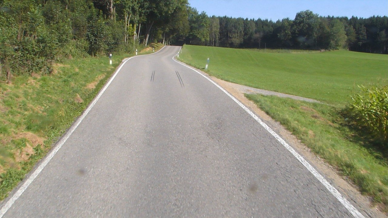 Das Foto zeigt die L 317 Arnach, die durch einen Wald führt. Rechts sieht man eine Wiese.
