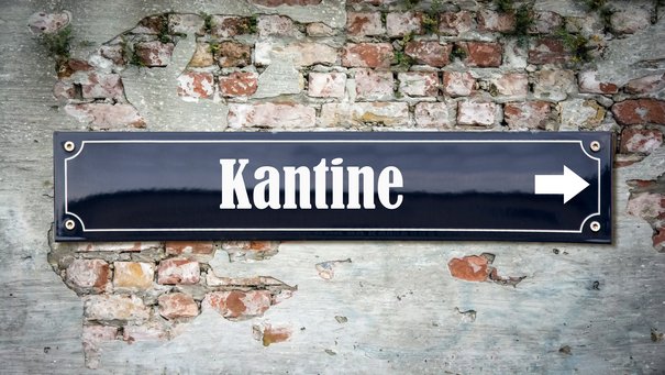 Schwarzes schmales Schild mit weißer Schrift Kantine auf Backsteinmauer