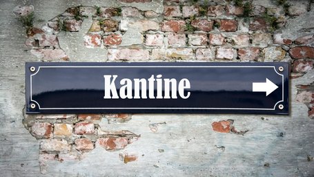 Schwarzes schmales Schild mit weißer Schrift Kantine auf Backsteinmauer