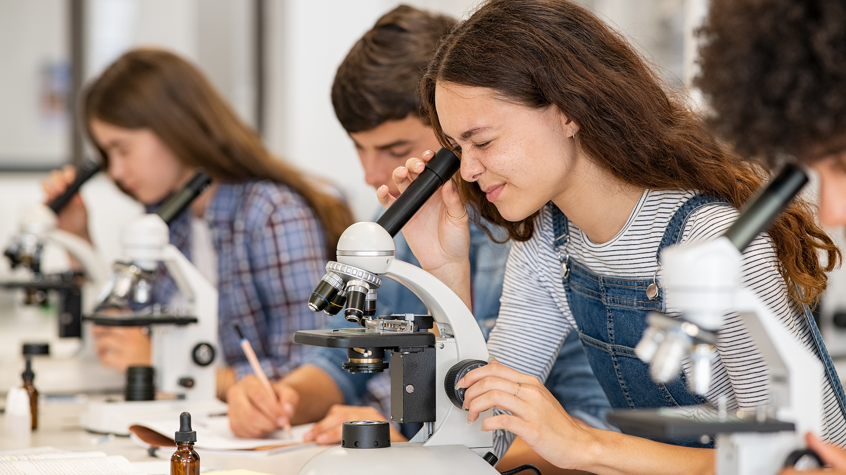 Biologieunterricht - Schülerinnen und Schüler sitzen an einem Tisch und schauen in Mikroskope