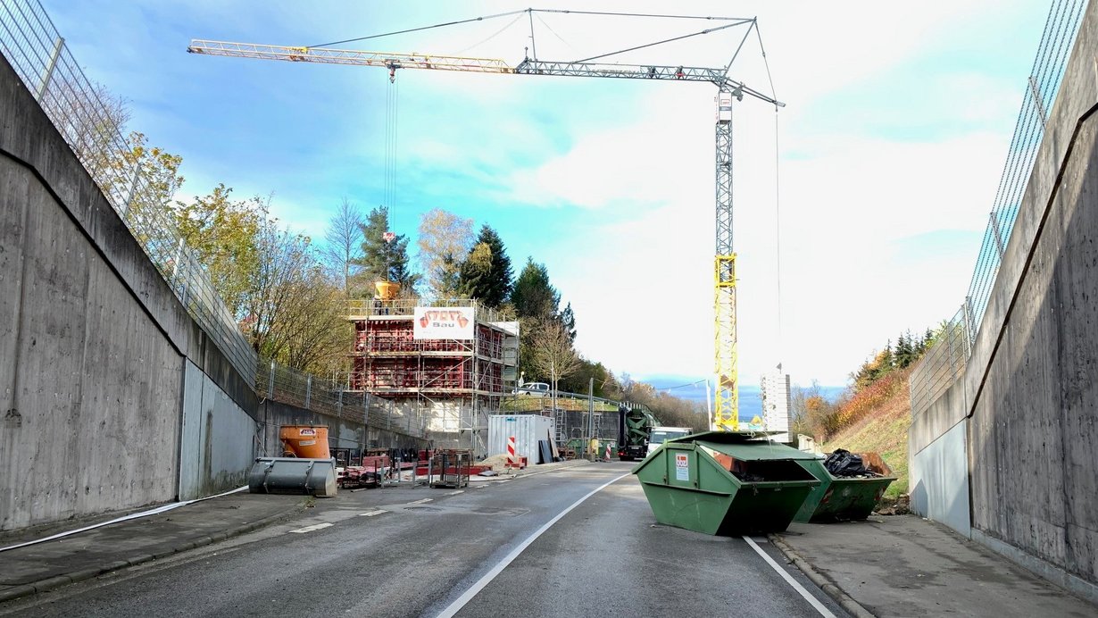 Ein Foto aus einem Tunnelportal heraus. Vor dem Tunnel stehen Baumaschinen und ein Kran.