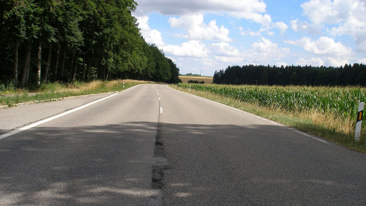 Das Bild zeigt ein gerades beschädigtes Stück der B 28; links sieht man eine Haltebucht und rechts ein Maisfeld