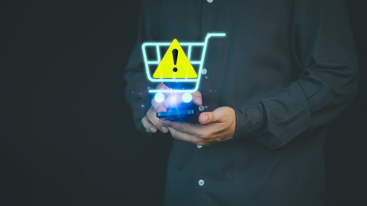AdobeStock_1238075113_Produktwarnung_ ParinPIX.jpeg Eine Hand hält einen kleinen Einkaufswagen in der Hand, darüber ist eine Warnzeichen gezogen.