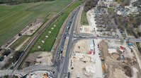 Luftbild einer Straßenbaustelle. Der Verkehr läuft auf einem Teil der vier Spuren, während auf beiden Seiten der Straße noch Bau-Aktivität herrscht.