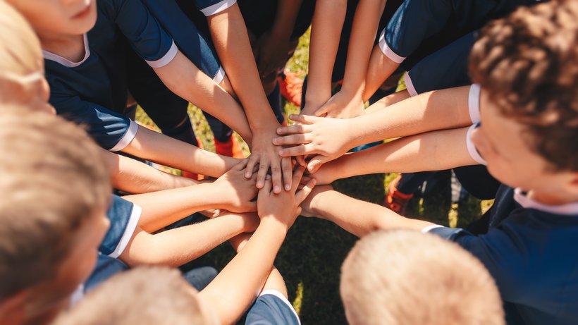 Eine Gruppe Jungs steht im Kreis zusammen und hält die Hände übereinander als Zeichen des Teambuildings