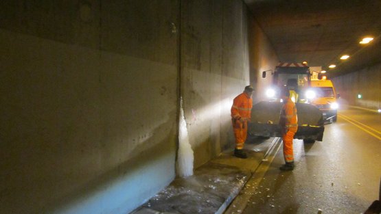 Bauarbeiter in einem Tunnel. Aus einer Fuge an der Tunnelwand quilt auf einer Höhe von einem Meter Eis.