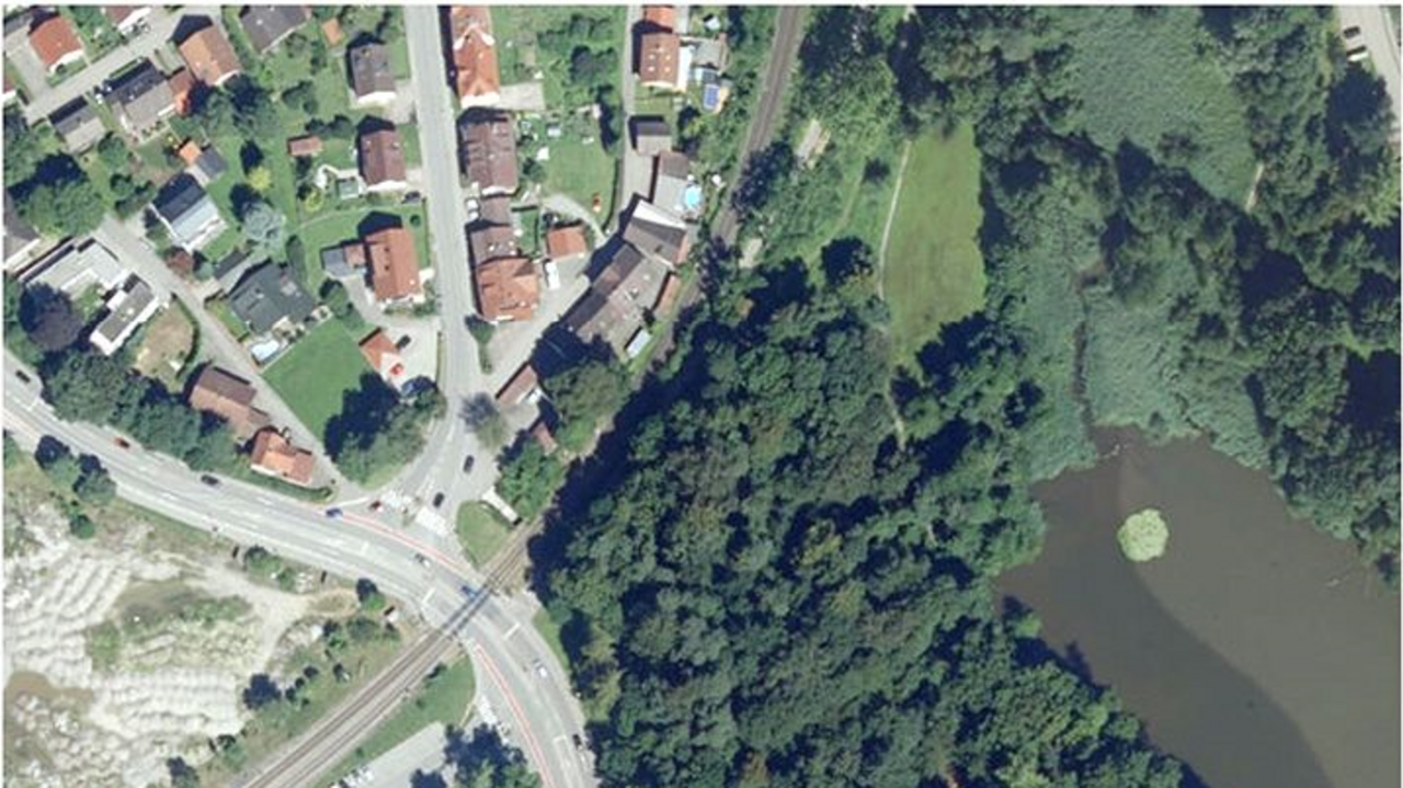 Luftbild; man sieht den Bahnübergang in Wangen, verschiedene Gebäude und ein Gewässer umrahmt von Bäumen