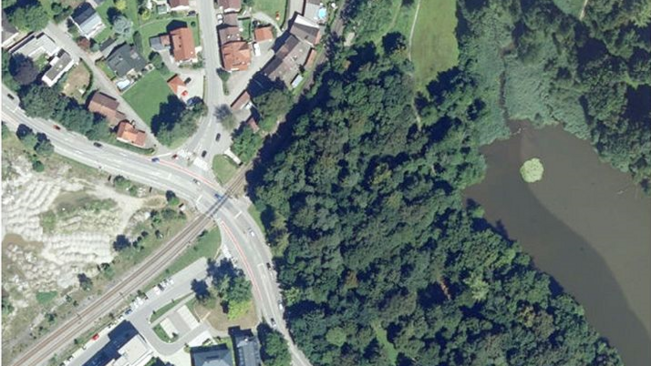 Luftbild; man sieht den Bahnübergang in Wangen, verschiedene Gebäude und ein Gewässer umrahmt von Bäumen
