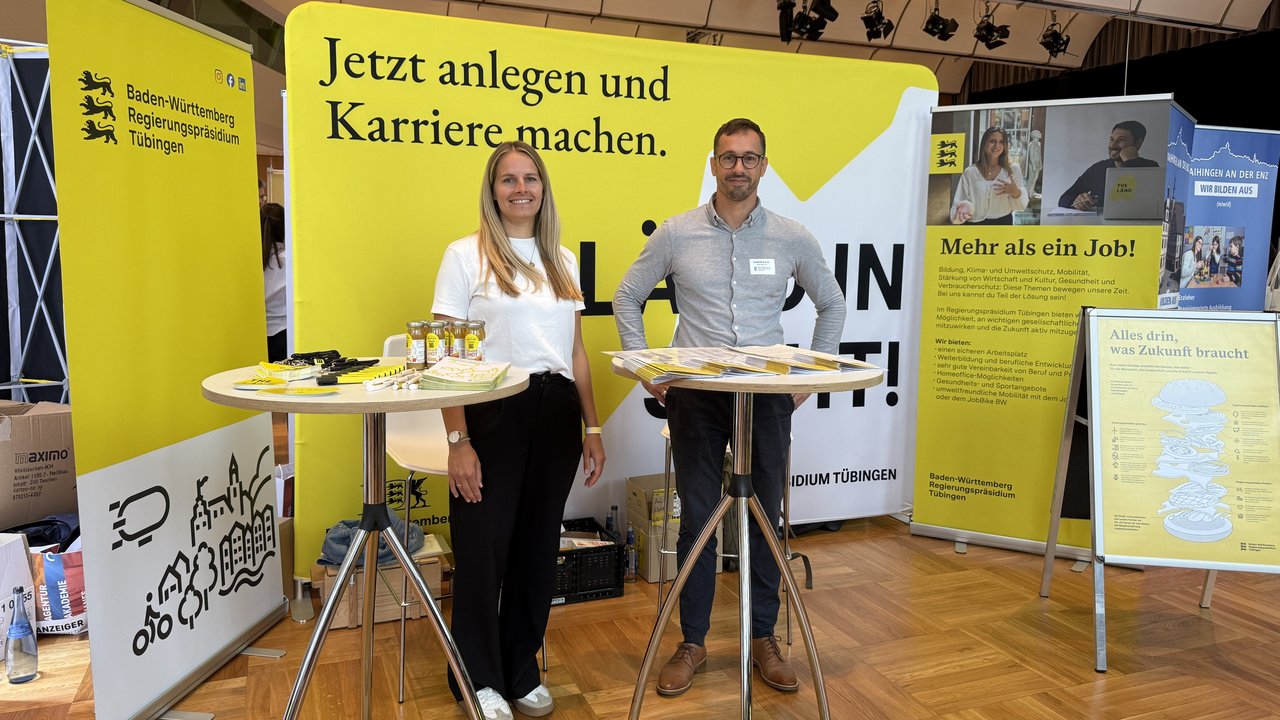 Zwei Männer stehen von einer Stellwand, auf der geschrieben steht: Anländen und Karriere machen beim Regierungspräsidium Tübingen