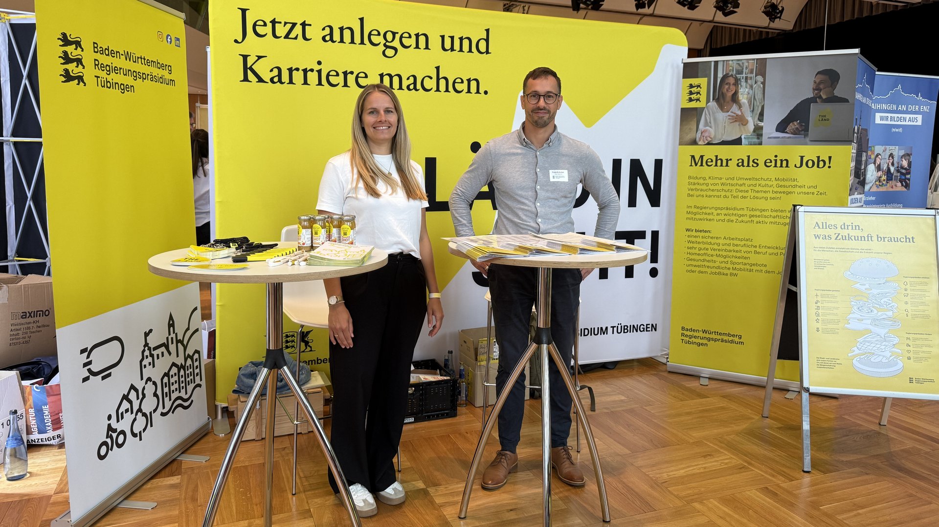 Zwei Männer stehen von einer Stellwand, auf der geschrieben steht: Anländen und Karriere machen beim Regierungspräsidium Tübingen