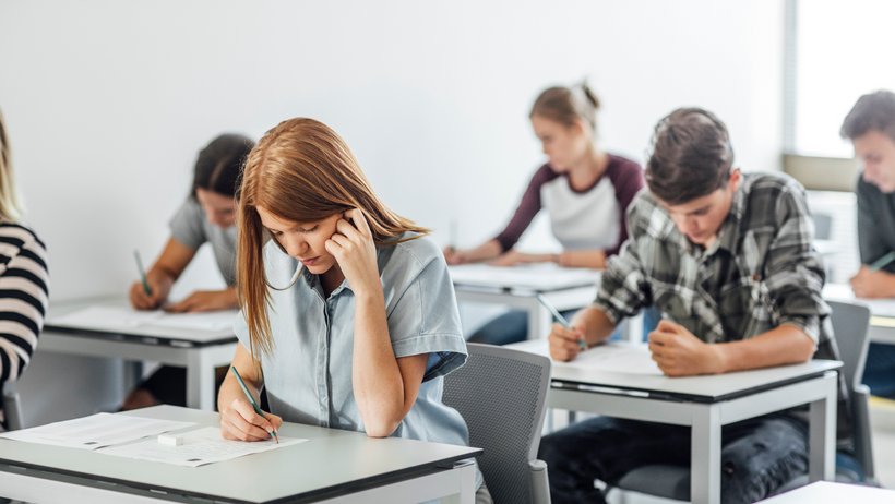 Schülerinnen und Schüler sitzen in einem Klassenraum und schreiben eine Prüfung.