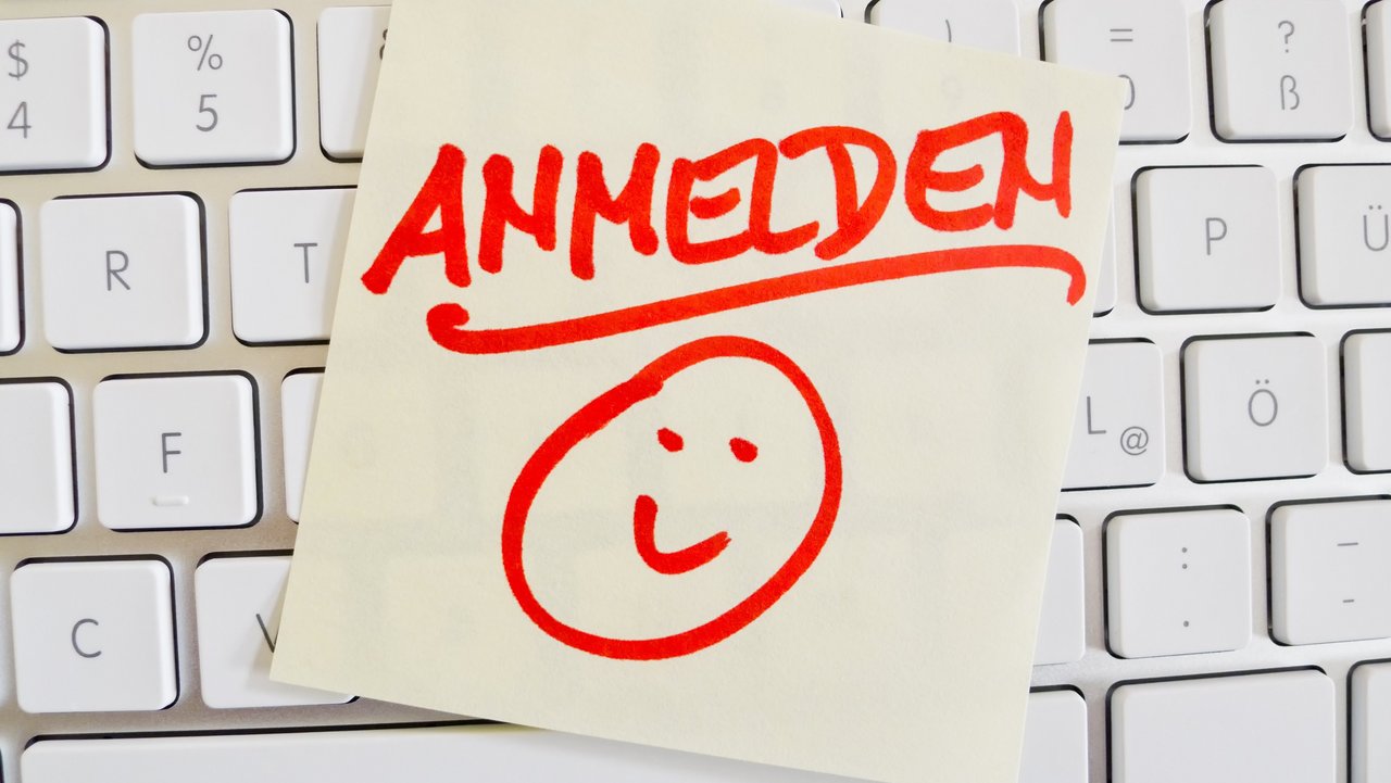 Auf einer Tastatur klebt ein gelber Button mit einem Smiley und einem riten Schriftzug "Anmelden"