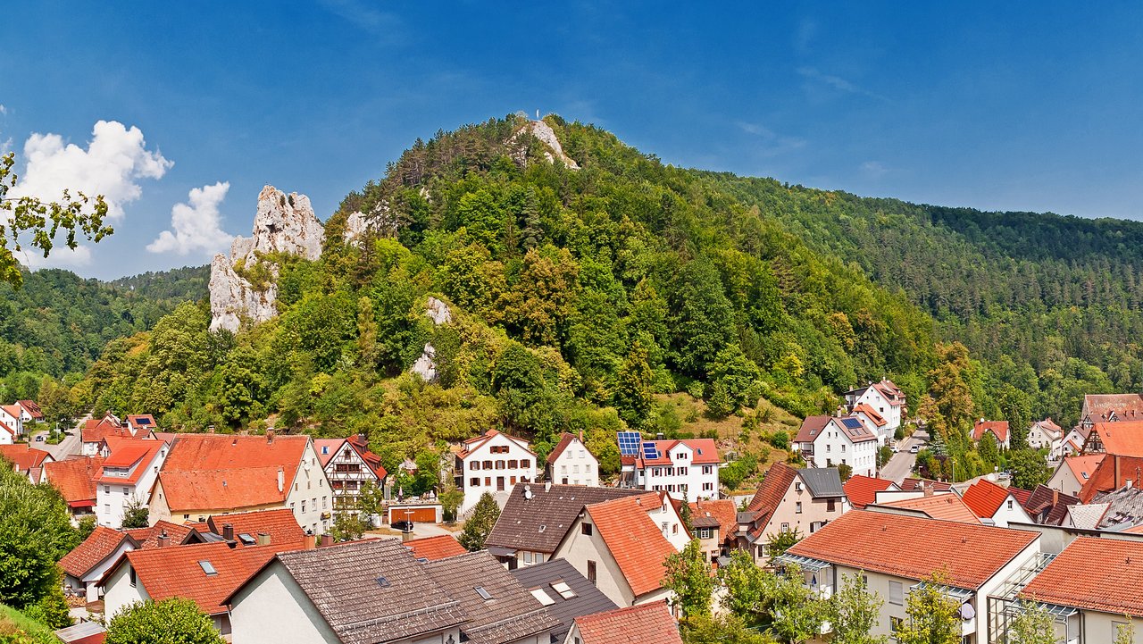 Blick von oben über die Stadt Blaubeuren, man sieht Dächer, umgeben von grünen Hügeln.