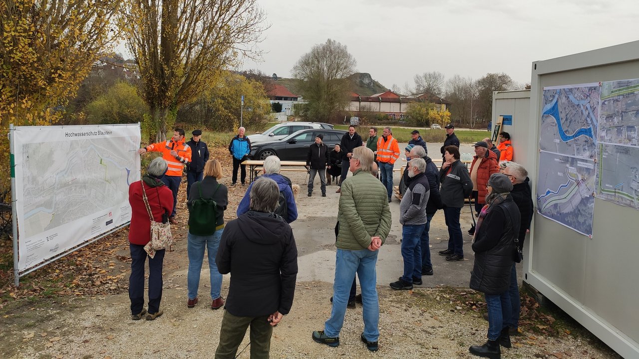 Das Foto zeigt Paolo Dapoz vom Ingenieurbüro Inros Lackner der anhand eines Übersichtslageplanes weiteren Personen die Hochwasserschutz-Maßnahmen erläutert