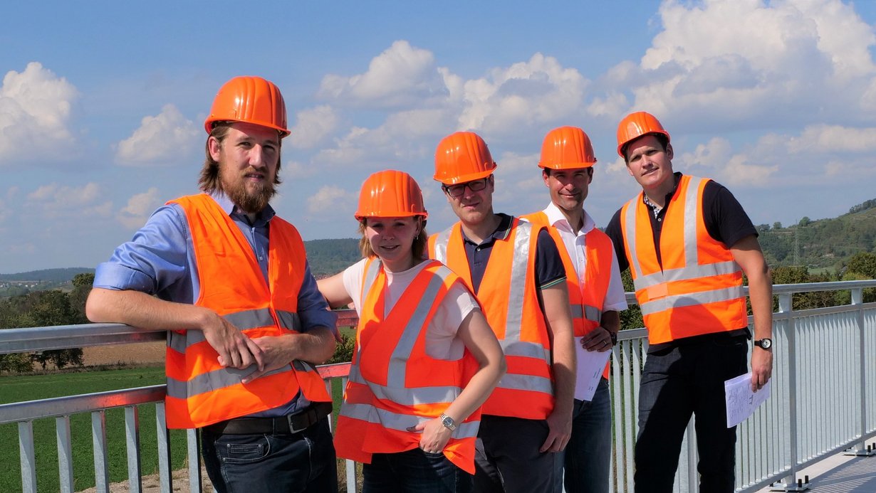 Referendare des Dualen Studiengangs "Bachelor of Engineering" stehen in Reihe hintereinander am Brückengeländer und lächeln in die Kamera