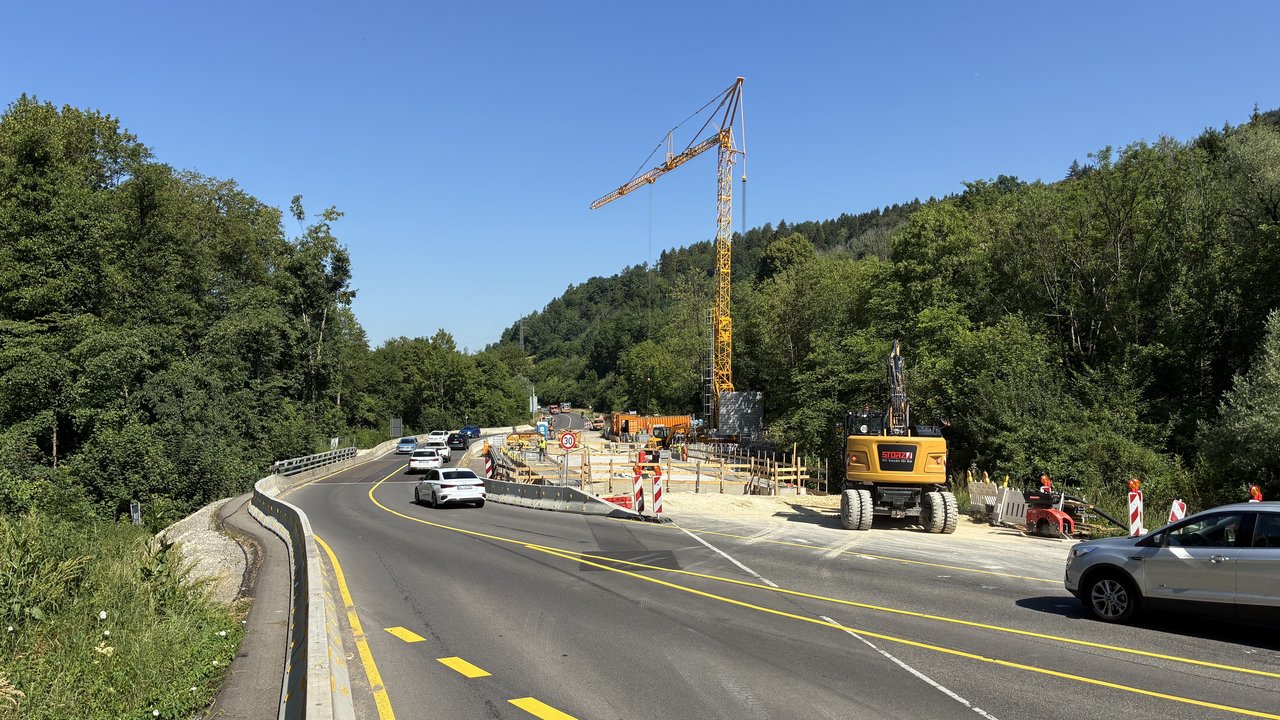 Das Foto zeigt die Baustelle auf der Brücke über die Eyach. Man sieht mehrere Baustellenfahrzeuge und einen Kran. Der Verkehr verläuft einspurig auf einer Umleitespur.