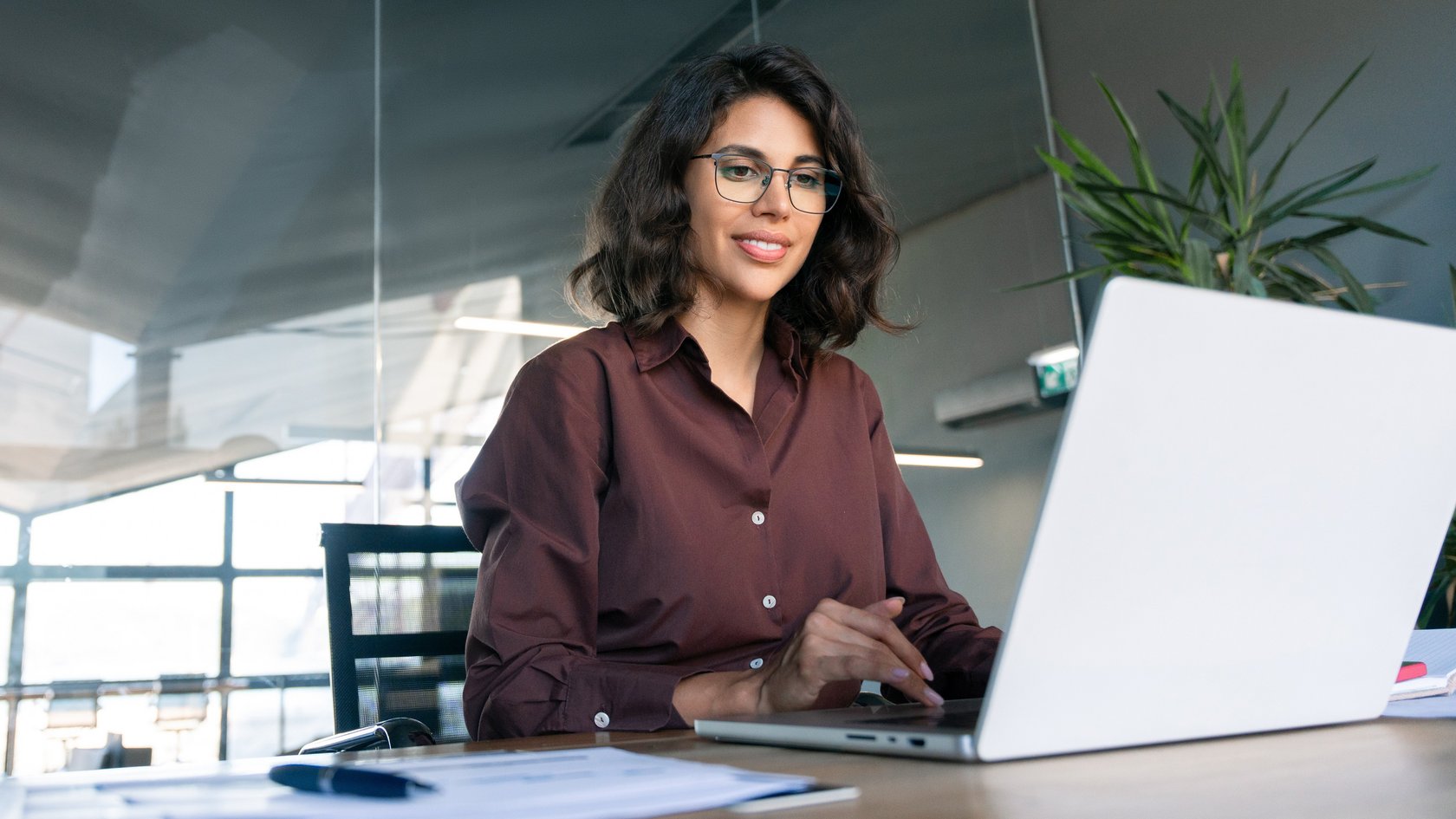 Eine junge Frau sitzt vor einem Laptop und lächelt in die Kamera.