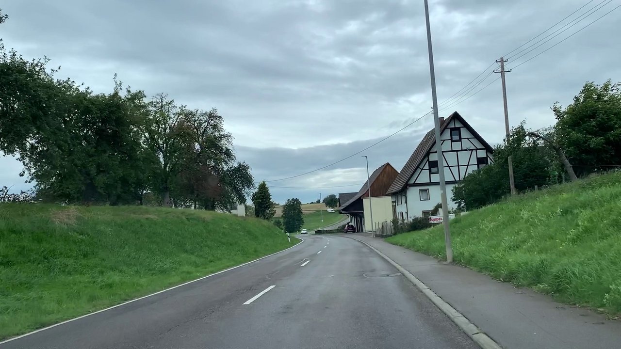 Das Bild zeigt die Landesstraße L 212. Rechts ein landwirtschaftliches Gebäude und links und rechts Wiesen und Bäume