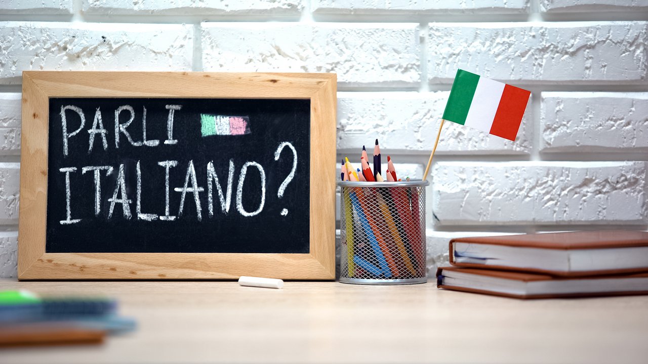 Sprechen Sie Italienisch Sprechen Sie Italienisch handschriftlich auf kleiner Tafel, italienische Flagge steckt in Box