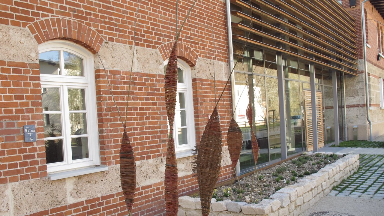Das Foto zeigt selbstgemachten Deko-Stelen aus Weide in Rabatten vor einem Backsteinhaus