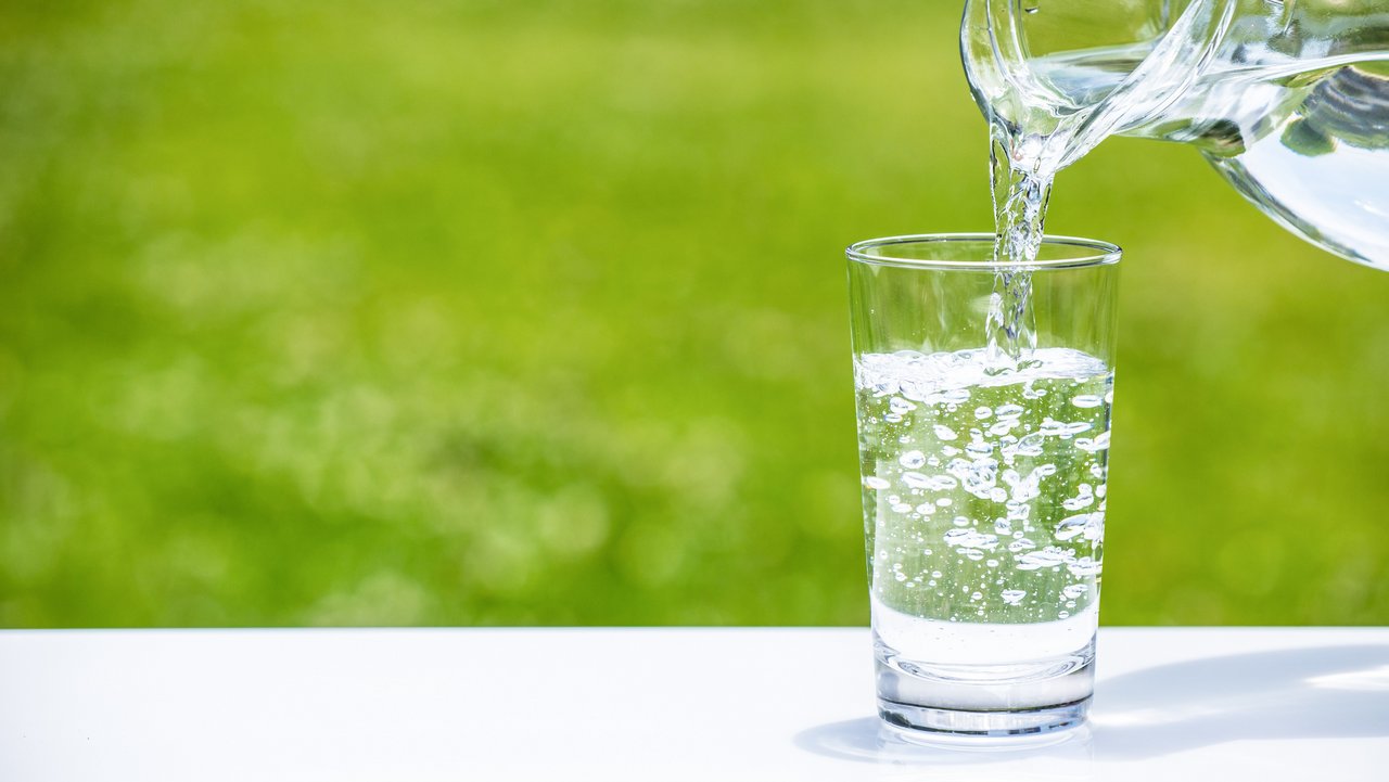 Aus einer Karaffe Wasser wird Wasser in ein Wasserglas gefüllt
