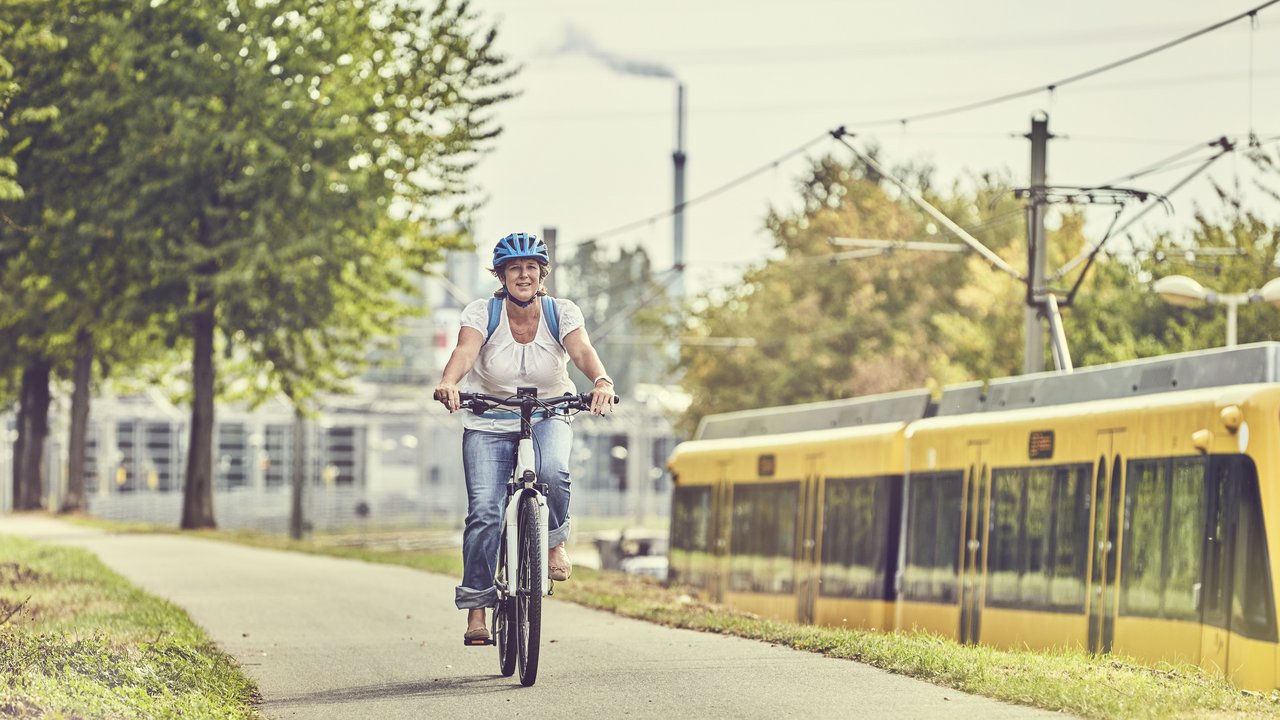 Frau auf einem Fahrad auf einem Radweg neben einer Bahnlinie