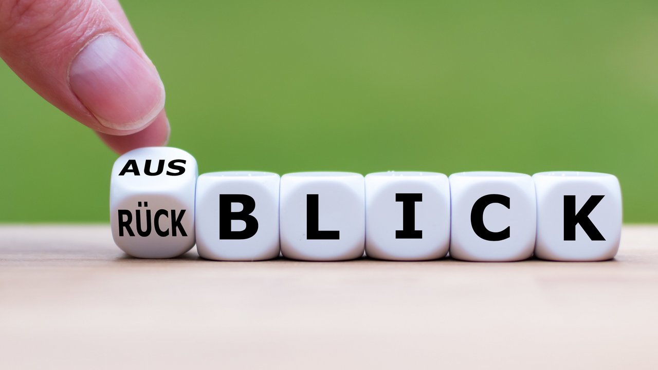 Würfel bilden das Wort Rückblick, ein Finger dreht den Würfel "Rück" auf "Aus"