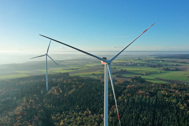 Man blickt über das Land Richtung Bodensee, im Vordergrund sind zwei Windkraftanlagen
