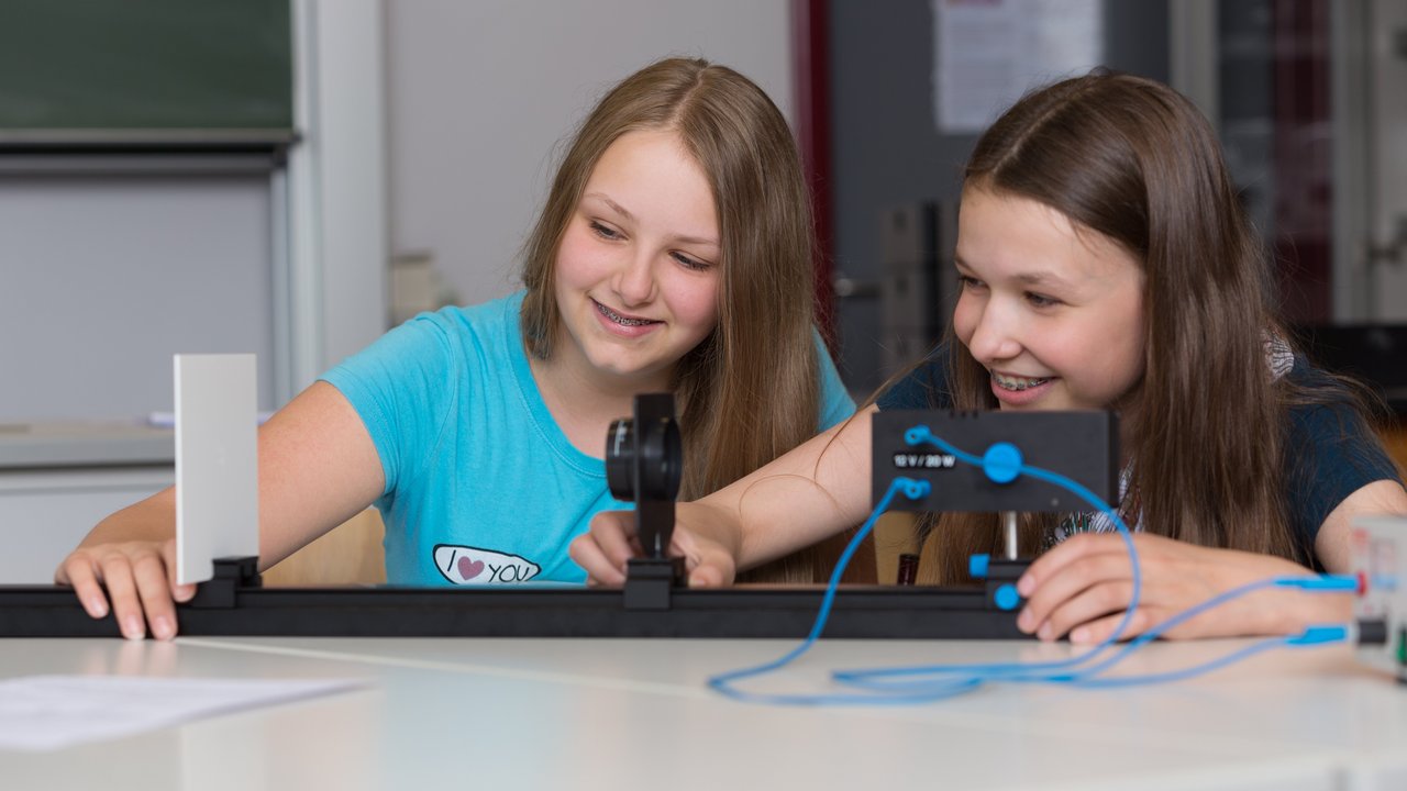 Unterrichtssituation NwT zwei schülerinnen sitzen am Tisch und bauen ein physikalisches Experiment zum Strahlensatz auf.