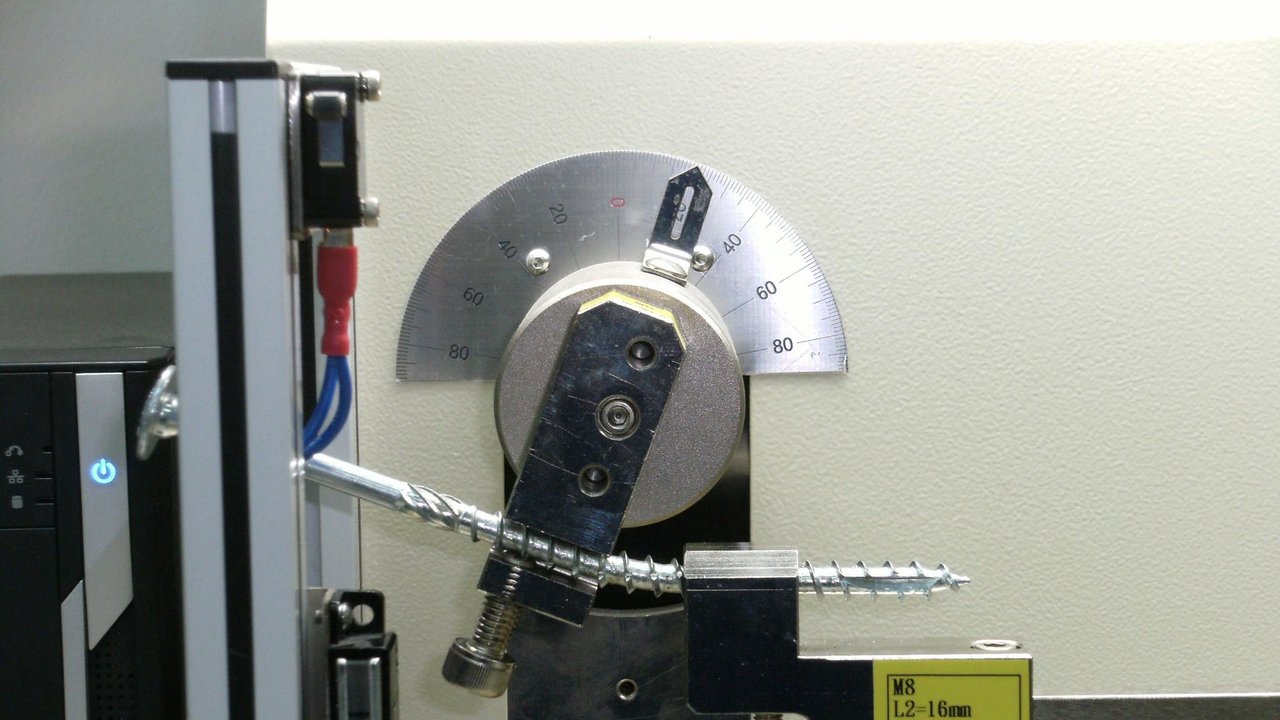 Eine Schraube für den Holzbau wird in einer Biegemaschine geprüft. Wenn die Schraube sich um einen bestimmten Winkel verbiegt, ohne an der Unterseite aufzureißen, hat sie den Test bestanden. 