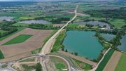 Eine Luftaufnahme, auf der eine neugebaute Straße, ein See und Felder zu sehen sind.
